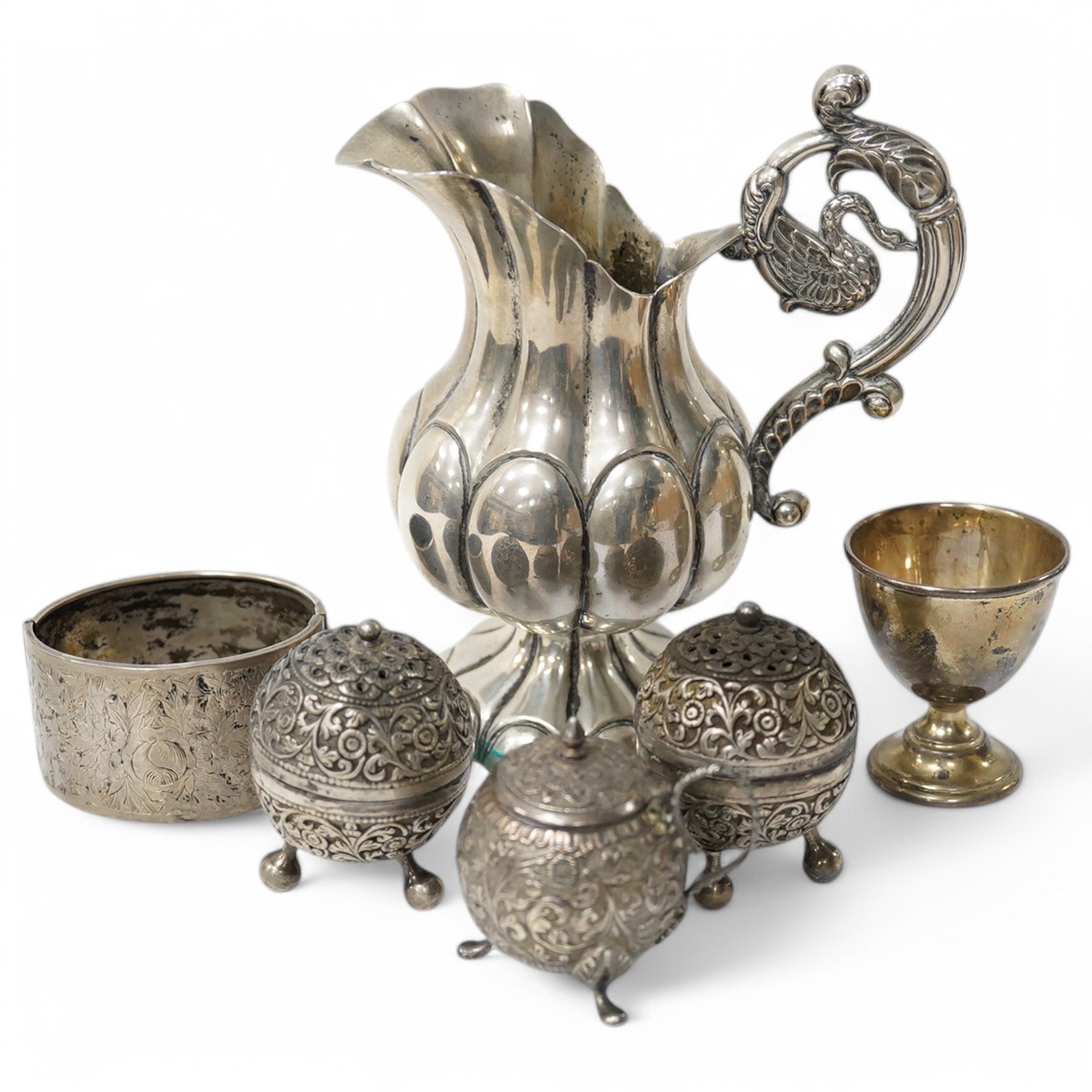 An Indian white metal three piece condiment set, a continental white metal jug, height 14cm, a silver egg cup and an engraved white metal hinged bangle. Condition - poor to fair